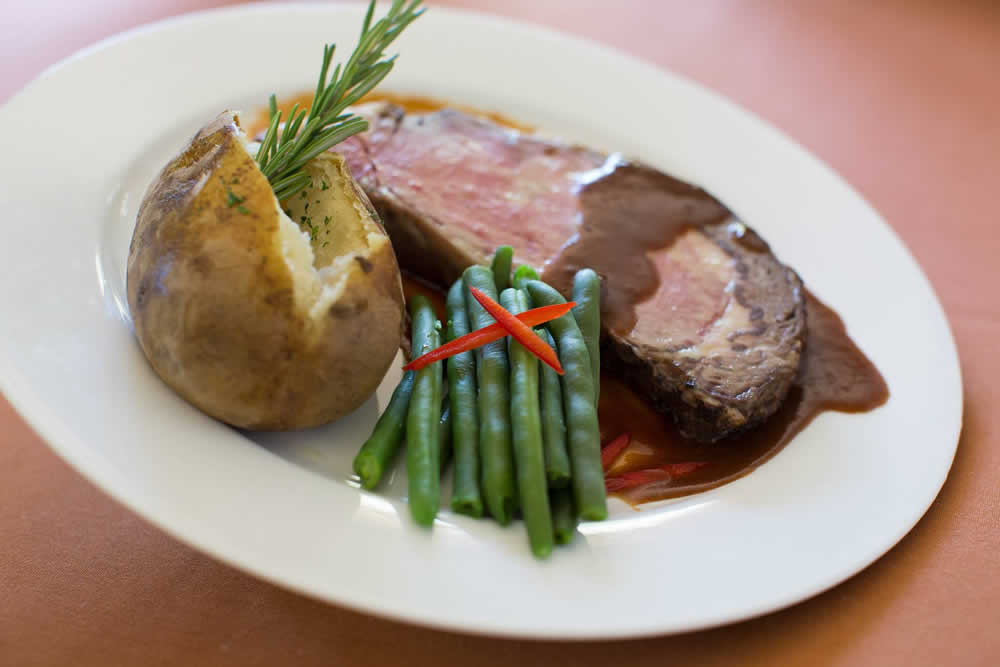 Close up of dinner plate with baked potato, steak and gravy, and green beans